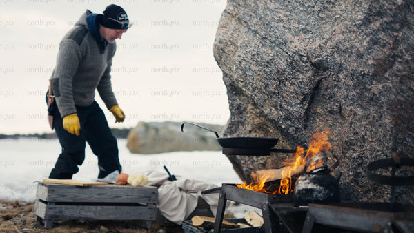 Winter cooking in the Luleå archipelago: Man prepares food by open fire