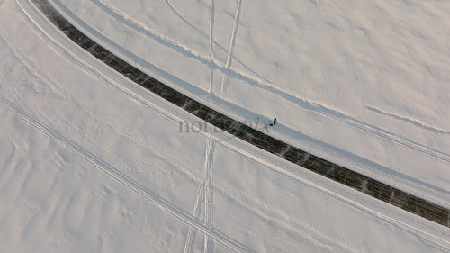 Flygfoto över person som promenerar hund på snöig väg i vinterlandskap, Luleå, Sverige