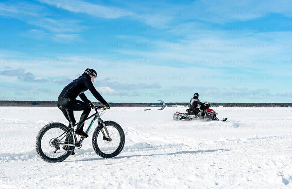 Cyclist and snowmobile on a frozen lake in winter