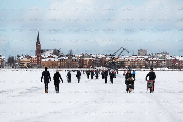 People walking on frozen river toward town skyline
