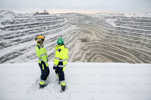 Two workers overlooking snowy open pit mine in winter