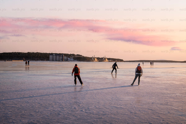 People ice skating on frozen sea at sunset