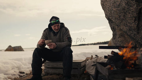 Man Enjoys Warm Drink by Bonfire on Snowy Beach in Luleå Archipelago, Winter