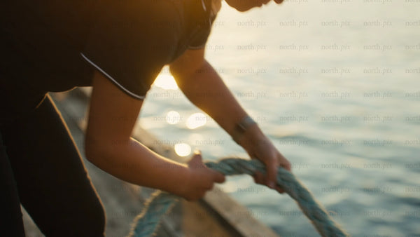Woman tying rope to mooring on wooden dock at sunset in Luleå