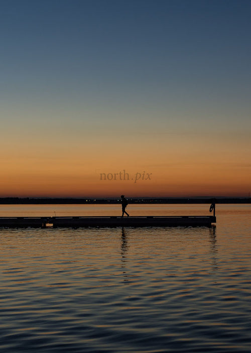 Person walking on pier at sunset