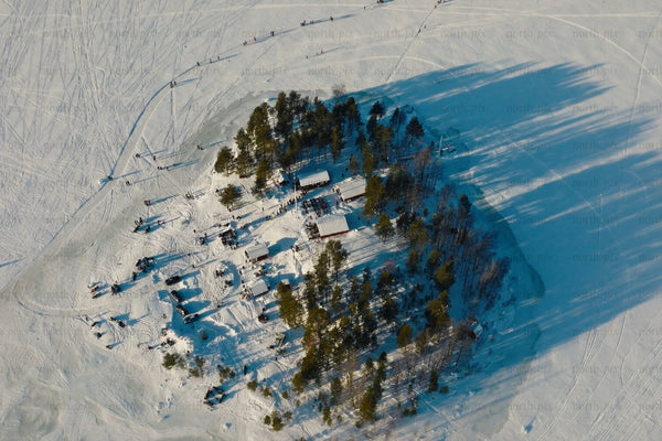 Aerial winter scene of snowy island village with trees and ski tracks