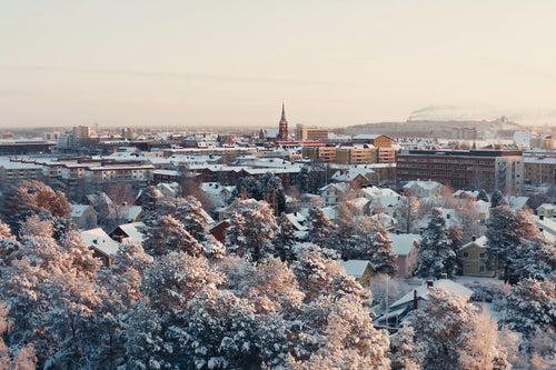Snöig stadskärna med utsikt över Luleå med träd, hus och vinterbelysning
