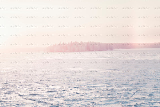 Frozen lake with distant tree-covered island at sunrise