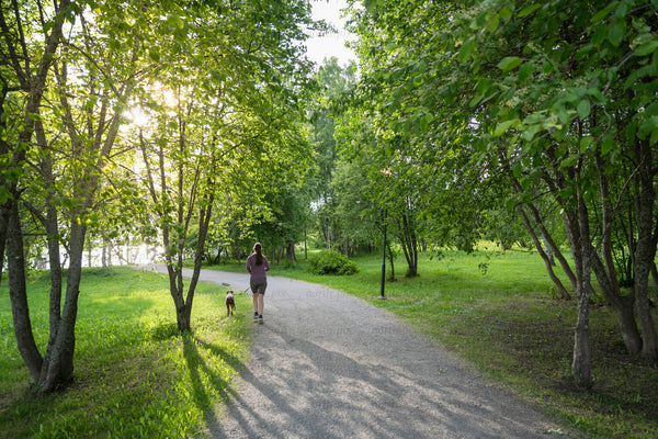 Woman walking dog on park path in evening light