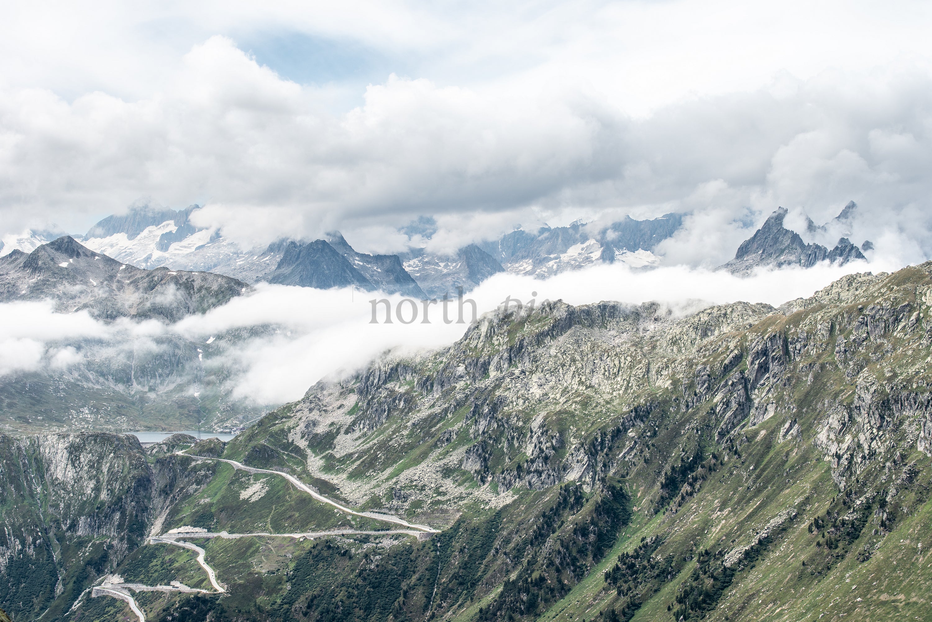 Winding mountain road through alpine ridges and clouds