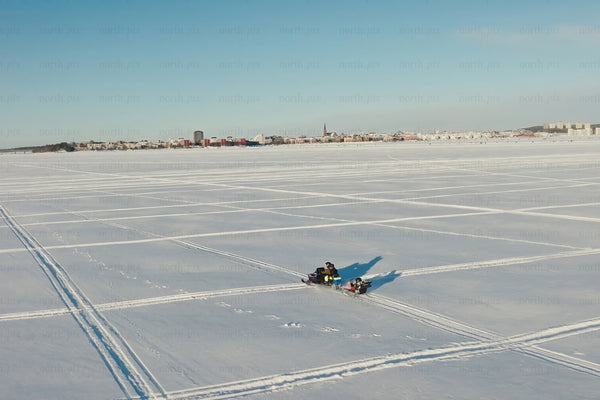 Snowy frozen lake with city skyline and snowmobiles under clear blue sky
