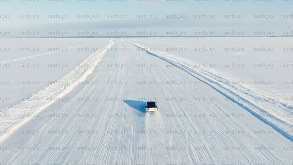 White Tesla/car driving on snowy ice road in Luleå, winter day, drone shot