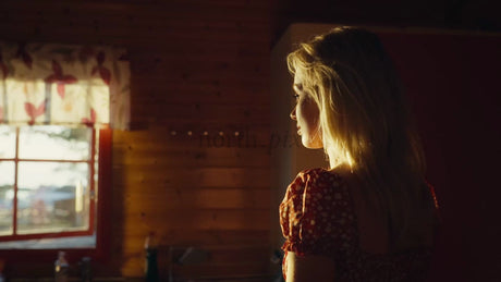 Woman Gazing Out Cabin Window During Golden Hour in Lulea, Sweden