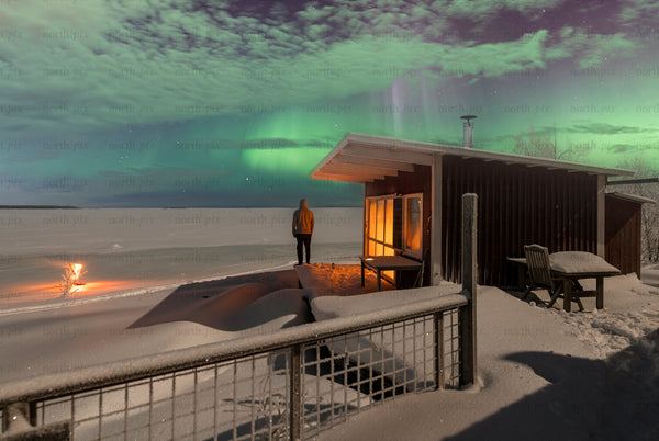 Person standing by cabin under northern lights at night