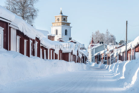 Snowy Street Lined With Traditional Red Wooden Houses and Church Tower in Winter Village