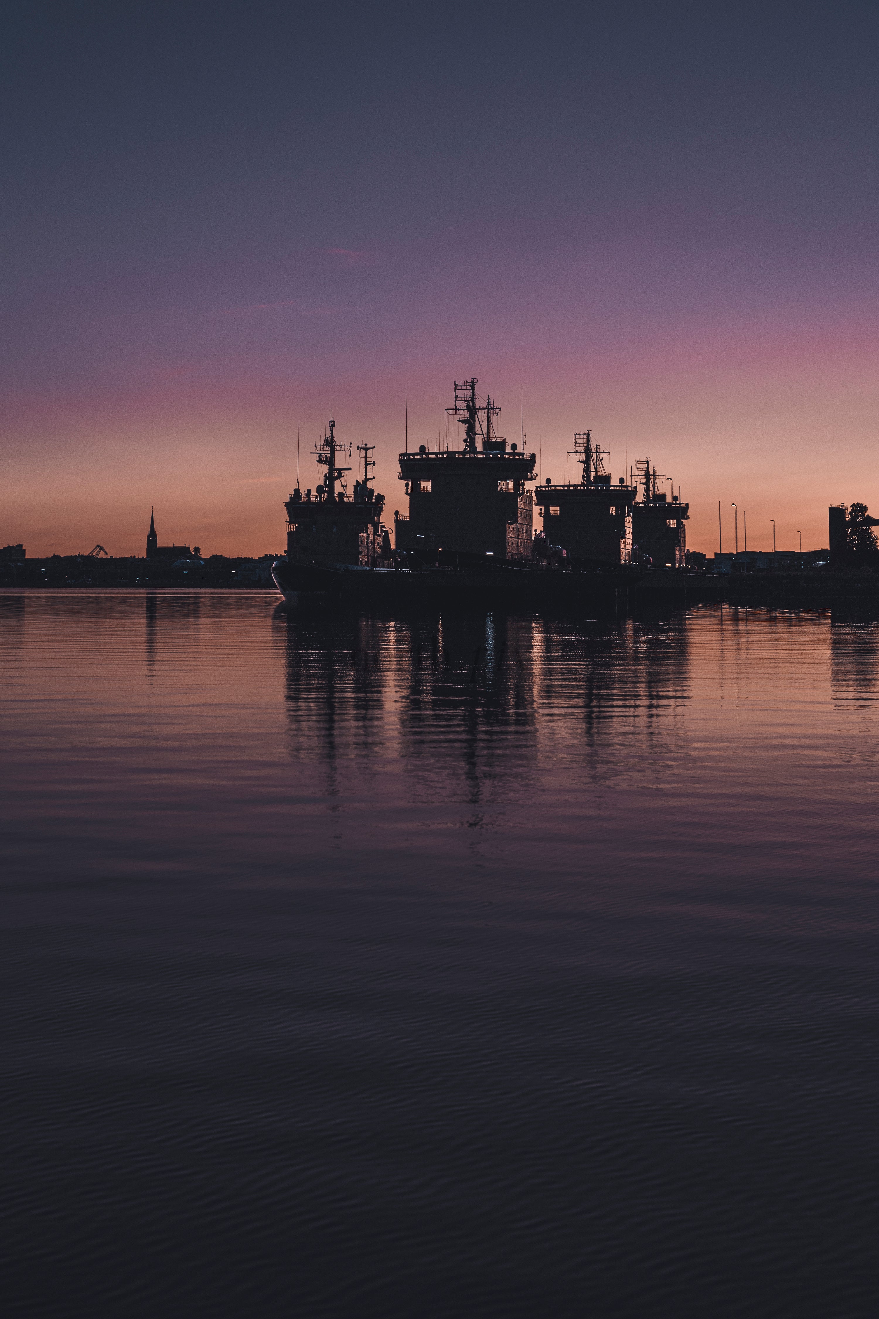 Silhouetted ships in harbor at dusk with reflections