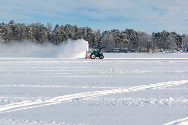 Winter snow field with tractor clearing snow on frozen lake near Luleå city center