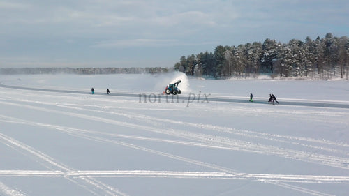 Traktor röjer snö på frusen sjö i Luleå, Sverige, med människor som åker skridskor och spark