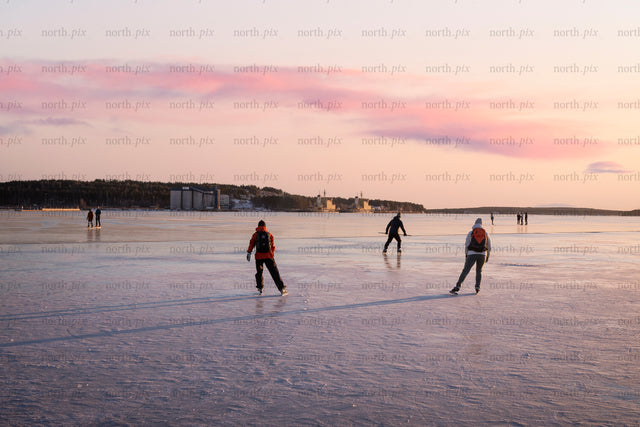 People ice skating on frozen sea at sunset