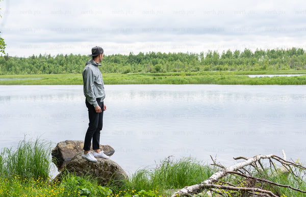 Man standing on rock by river under cloudy sky