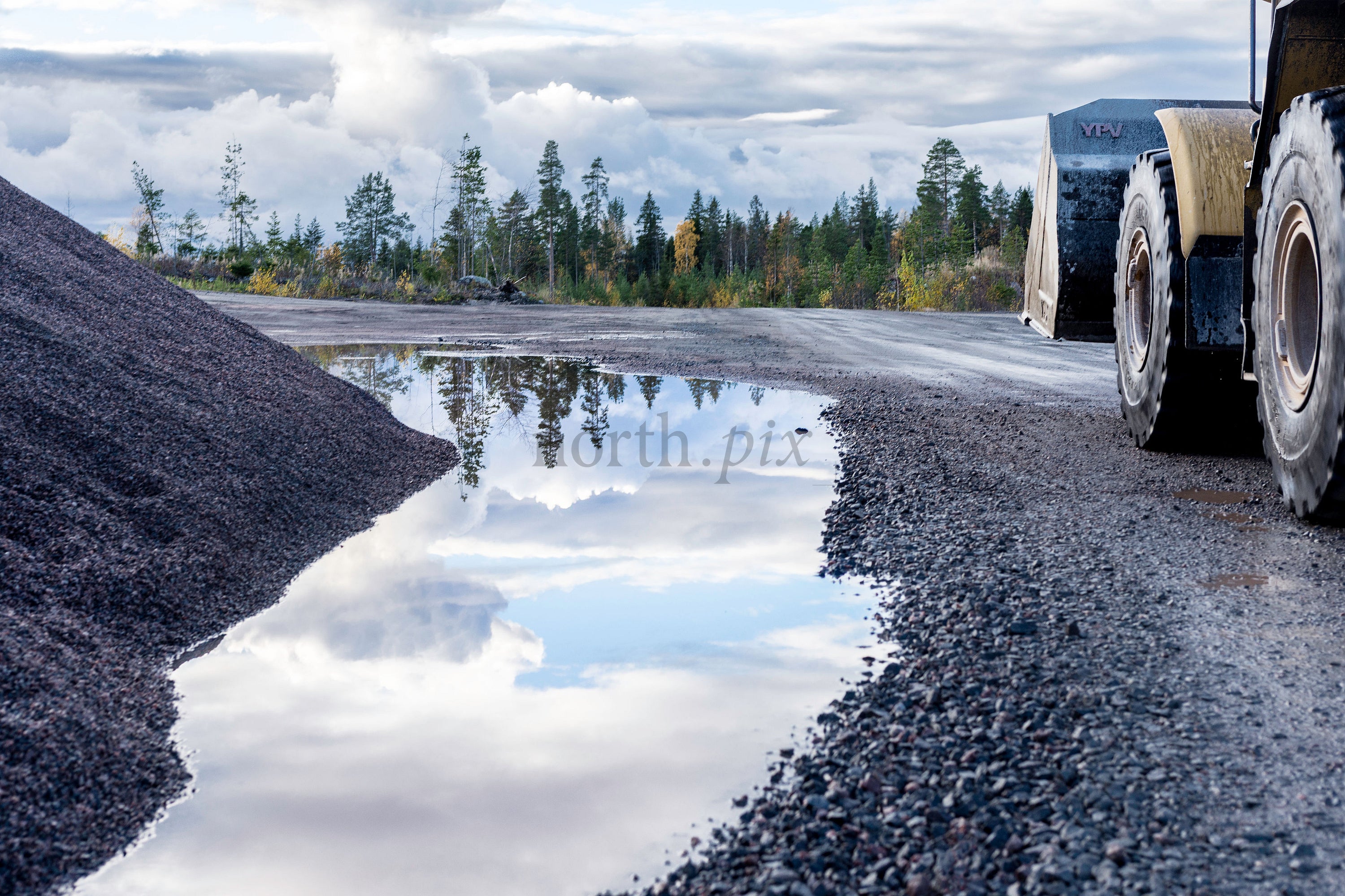 Wheel loader and gravel pile on wet gravel road, autumn