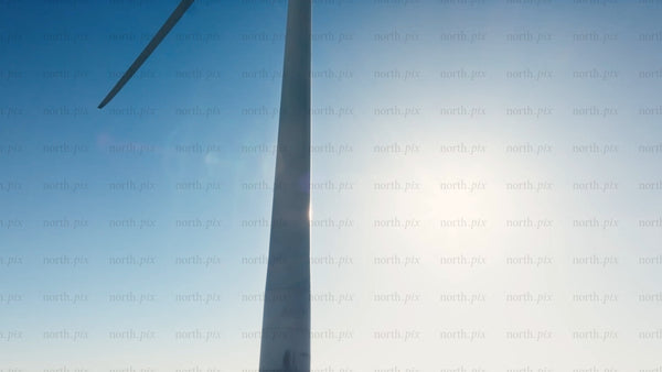 Rotating wind turbine against blue sky and sun: Zoom out to snowy winter landscape of Markbygden wind farm, Sweden