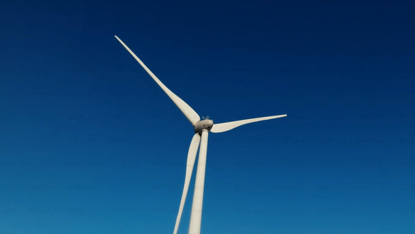 Wind turbine rotating against a clear blue sky in a winter landscape