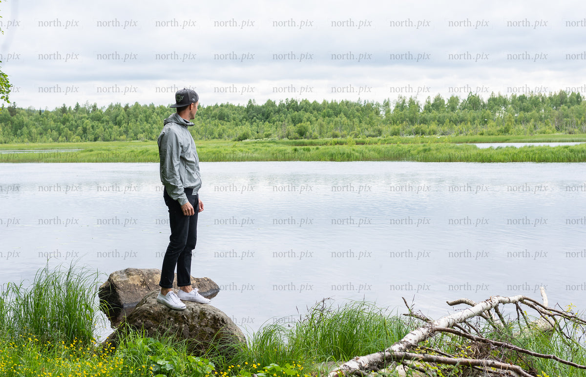 Man standing on rock by river under cloudy sky