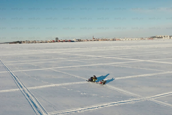 Snowy frozen lake with city skyline and snowmobiles under clear blue sky