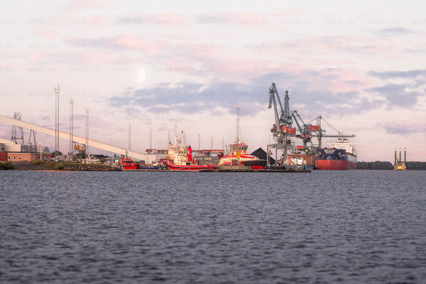 Cargo ship and cranes at industrial harbor at dusk