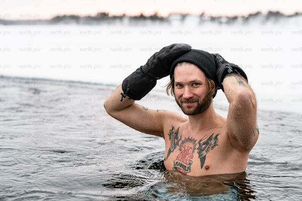Man in icy water wearing beanie and mittens, winter