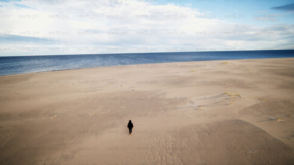 Lone person walks on sandy beach toward ocean in Luleå, summer day drone shot