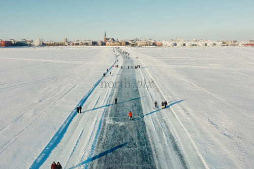Isstig över snötäckt sjö mot Luleå centrum med åkare och snötäckt skyline