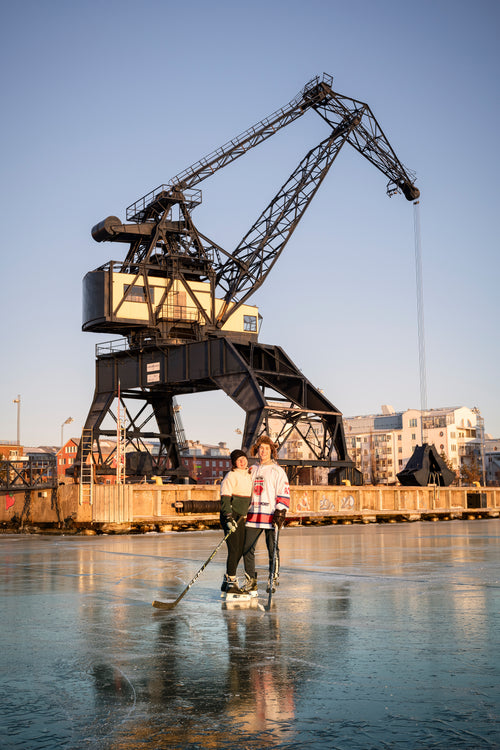 Two people playing ice hockey by harbor crane at sunset