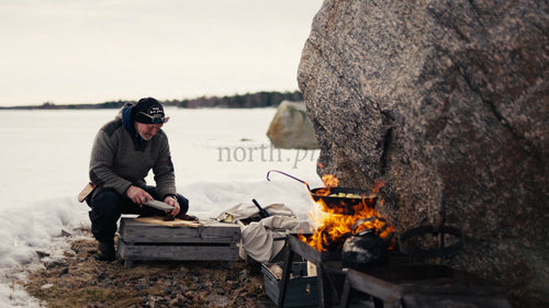 Man som lagar mat över öppen eld, vinterdag i Luleå skärgård, Sverige