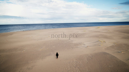 Ensam person går på sandstrand mot havet i Luleå, Sverige, drönarbild från sommardag
