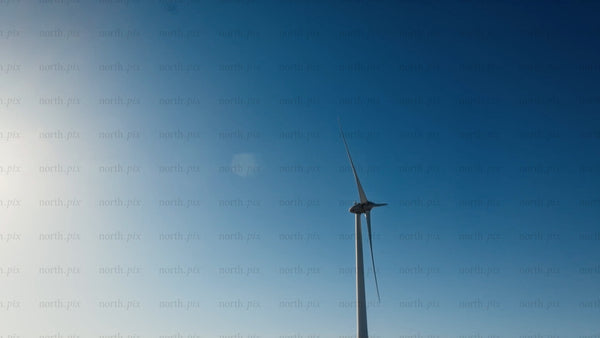 Wind turbine rotating against blue sky with sun, low angle view in winter
