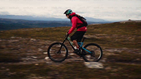 Mountain biker in red jacket riding downhill on rocky hillside
