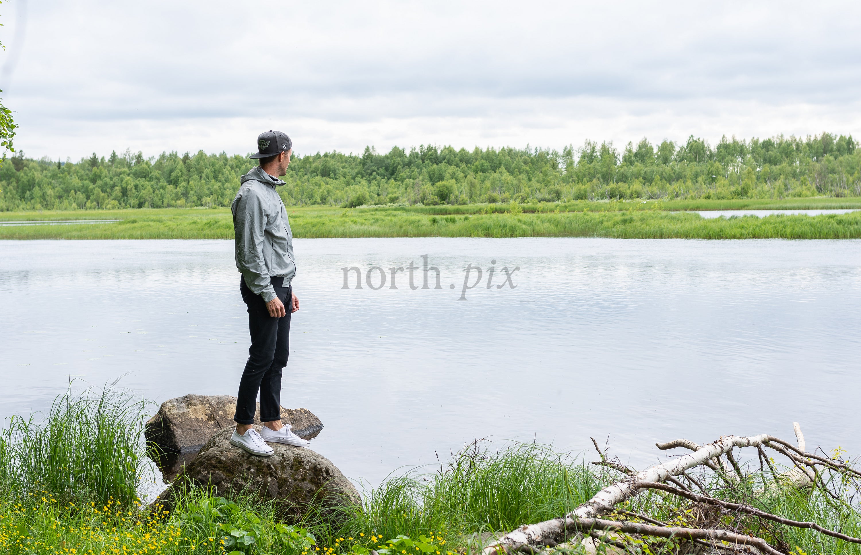 Man standing on rock by river under cloudy sky
