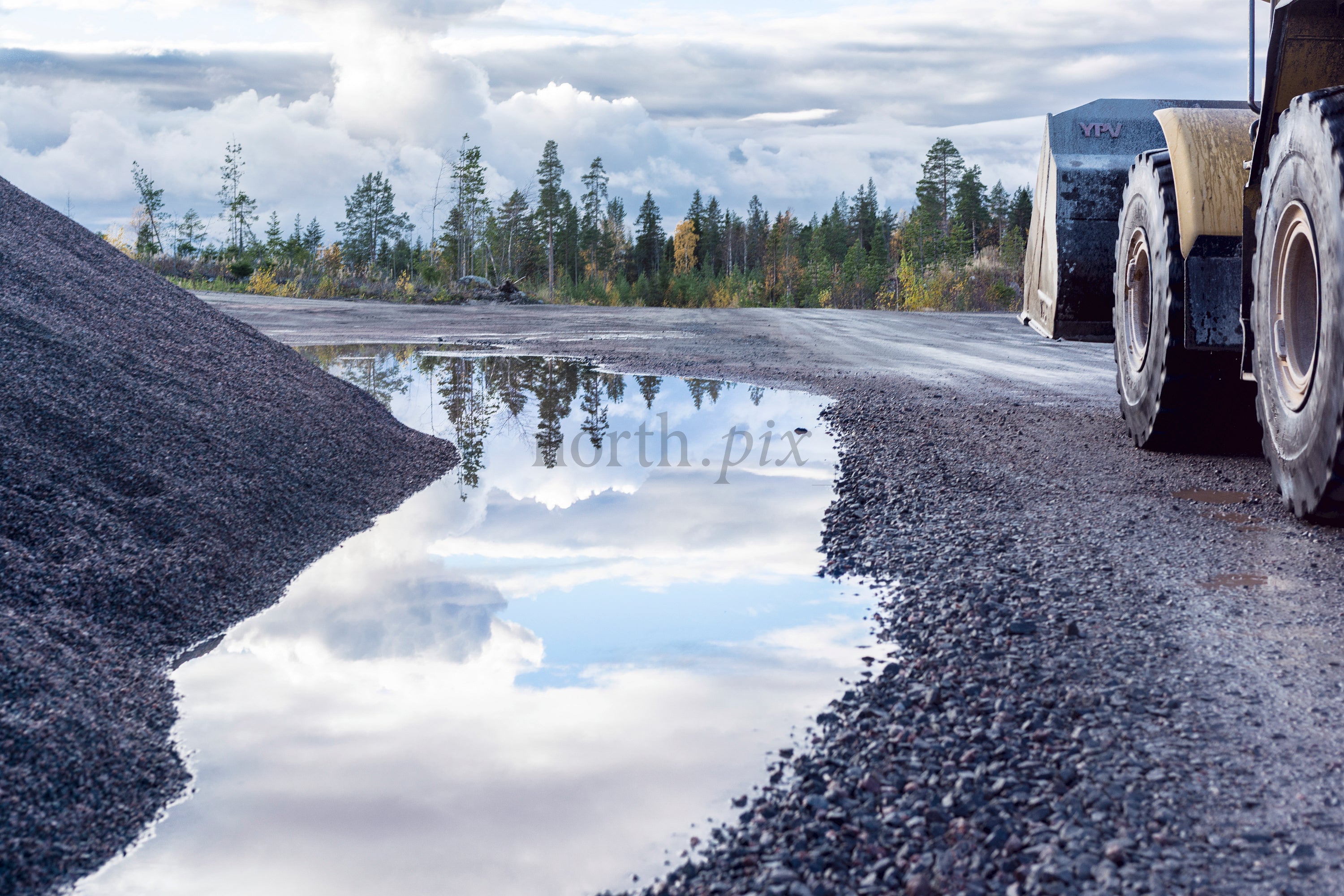 Wheel loader beside gravel pile and puddle, autumn