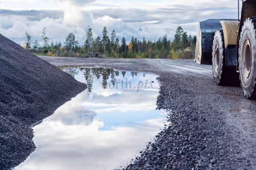 Wheel loader beside gravel pile and puddle, autumn