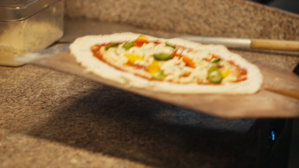 Chef places pizza in wood-fired oven, close-up