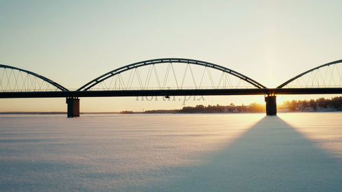 Vintersolnedgång över frusen flod och bro i Luleå, Sverige: Flygfoto från drönare