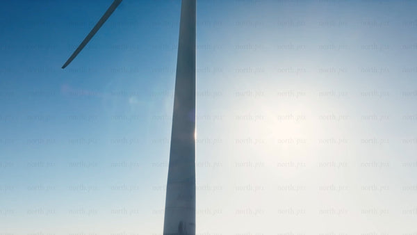 Rotating wind turbine against blue sky and sun: Zoom out to snowy winter landscape of Markbygden wind farm, Sweden