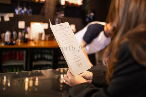 Person reading a menu at a bar counter in evening