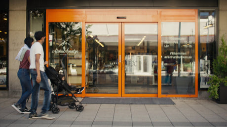 Family with Baby Stroller Entering Store in Luleå, Sweden on a Summer Day