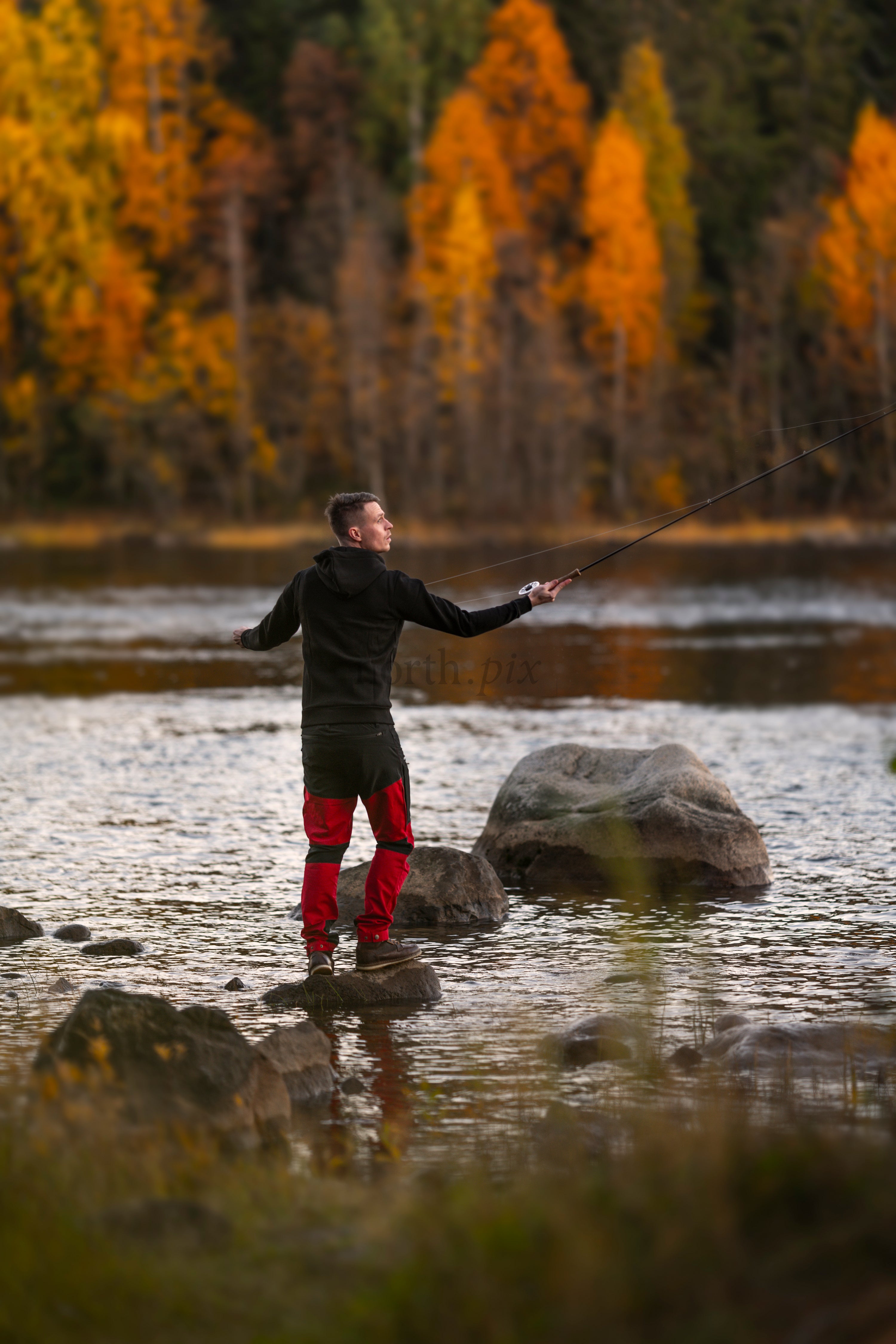 Man fly fishing on river with autumn forest