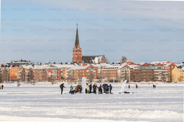 People on a frozen lake with town skyline, winter morning
