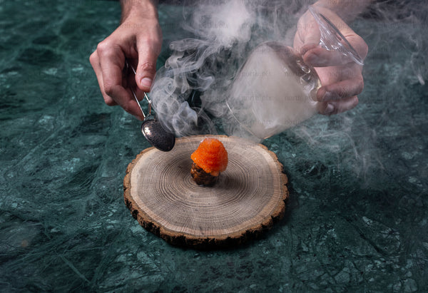 Hands smoking an appetizer on a wood slice