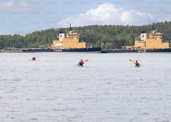 Kayakers paddling near docked icebreakers on overcast day